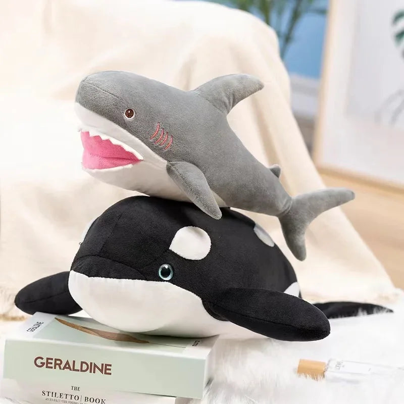 A plush stuffed animal depicting a great white shark and a dolphin, resting on a book.