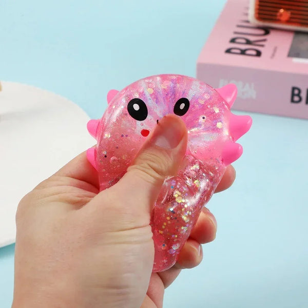 A hand holds a pink, glittery axolotl squishy sensory fidget toy against a light blue background.
