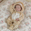 A realistic vinyl reborn baby doll wearing a tan bear outfit sleeping on a floral patterned blanket.