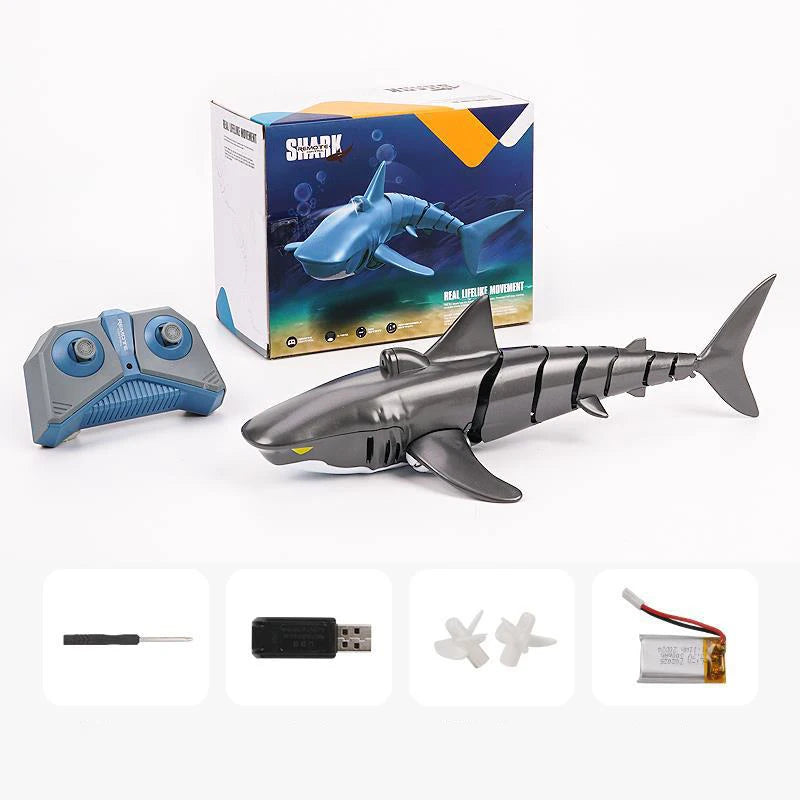 A gray shark toy is shown next to its packaging box and various accessories for a remote control shark toy.