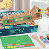A wooden crocodile test tube clip toy with colorful beads and a yellow hand gesture, displayed on a box.