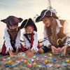 Three children dressed as pirates are laying out colorful acrylic gemstones on the ground.