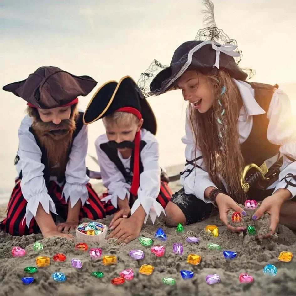 Three children dressed as pirates are laying out colorful acrylic gemstones on the ground.