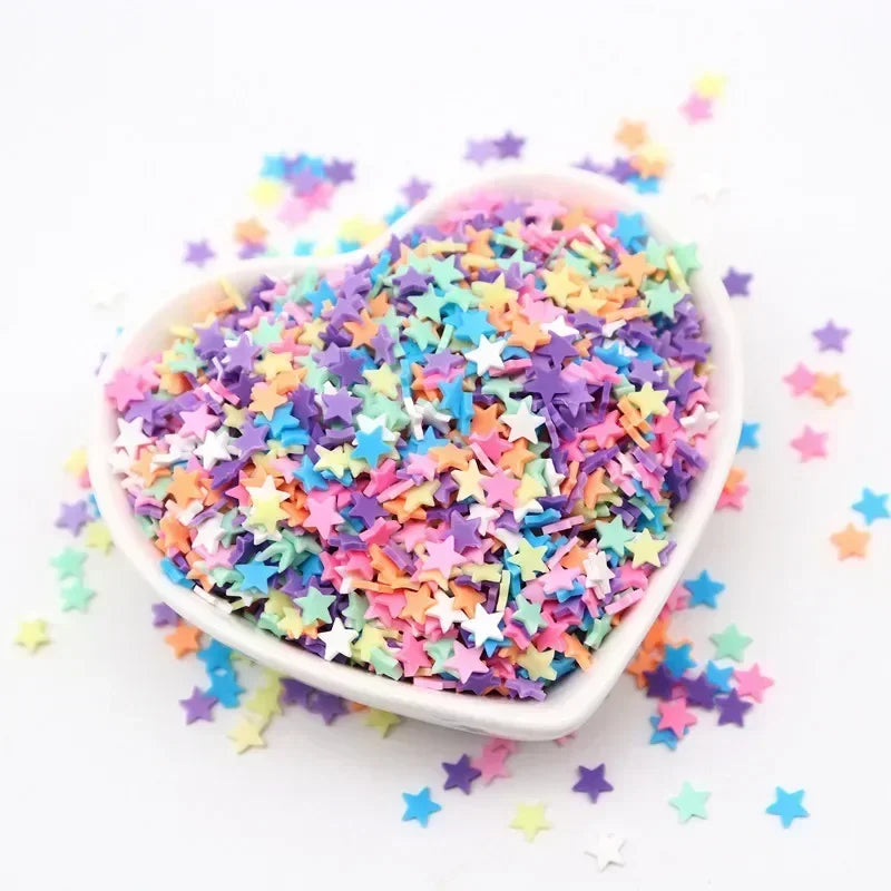 A bowl filled with colorful polymer clay sprinkles in various star shapes scattered on a white background.