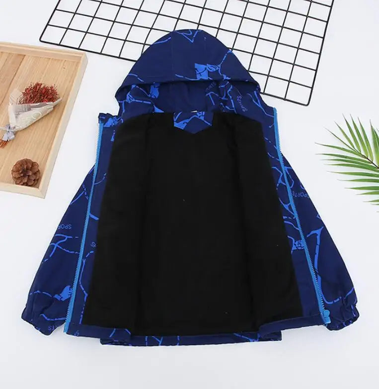 A dark blue waterproof winter jacket with a hood laid flat on a white background next to a grid and a green leaf.