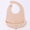 A light beige waterproof silicone baby bib with a catch pocket and multiple holes for fastening.