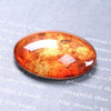 A close-up of a round amber craft doll eye with a glitter finish resting on a gray textured background.
