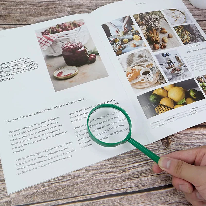 A hand holds a green magnifying glass over a page of an educational book featuring nature and food items.