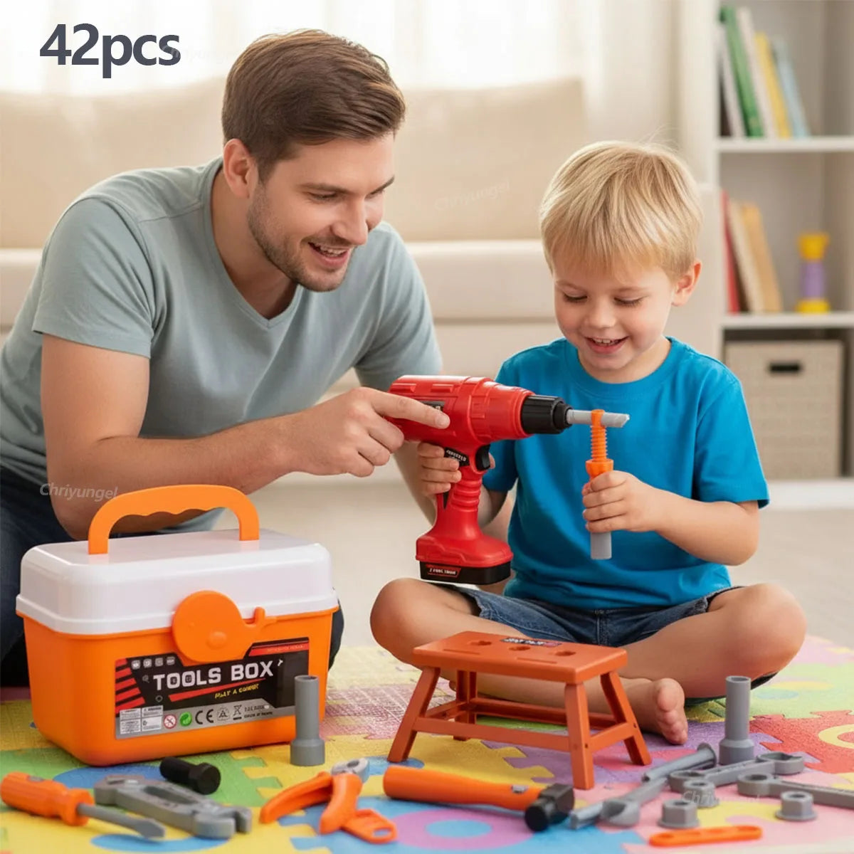 A boy and man are playing with an orange electric drill tool set and various plastic tools on a colorful mat.