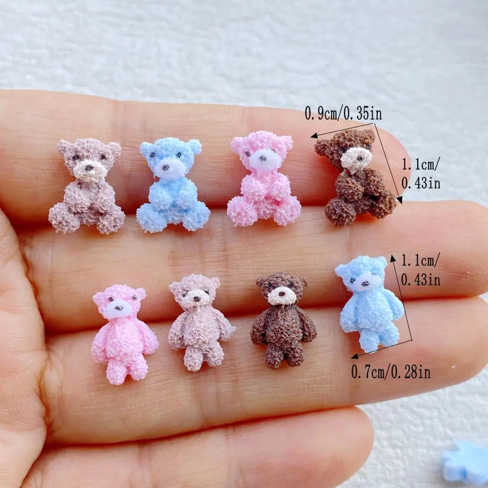 A collection of mini resin teddy bear charms in various pastel colors, including pink, blue, and brown, displayed on a hand.