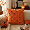 An orange textured pillow with black ghost designs sits on a light-colored sofa next to a carved pumpkin.