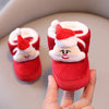 A hand holds a pair of soft, red baby winter boots with white and red Santa-themed trim.