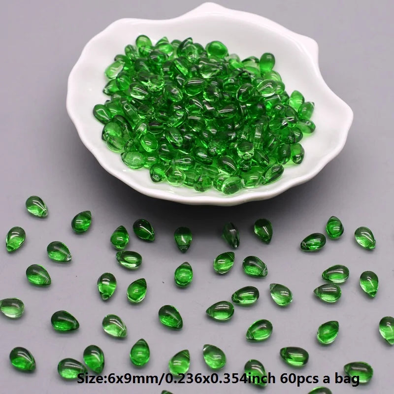 A white dish filled with green water drop glass beads for jewelry making
