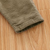Close-up of olive green baby cotton overalls with ribbed fabric lying on a wooden surface.
