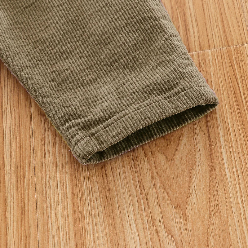 Close-up of olive green baby cotton overalls with ribbed fabric lying on a wooden surface.