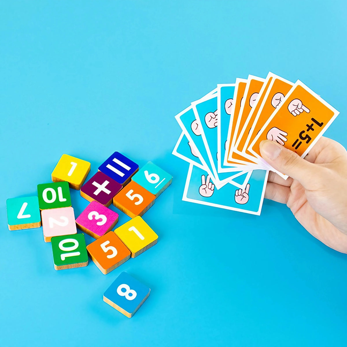 A hand holds a stack of orange cards showing finger counting and several wooden blocks with numbers 0 through 8.