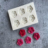 A white silicone mold with six rose flower shapes for candle and soap making is displayed on a gray surface.