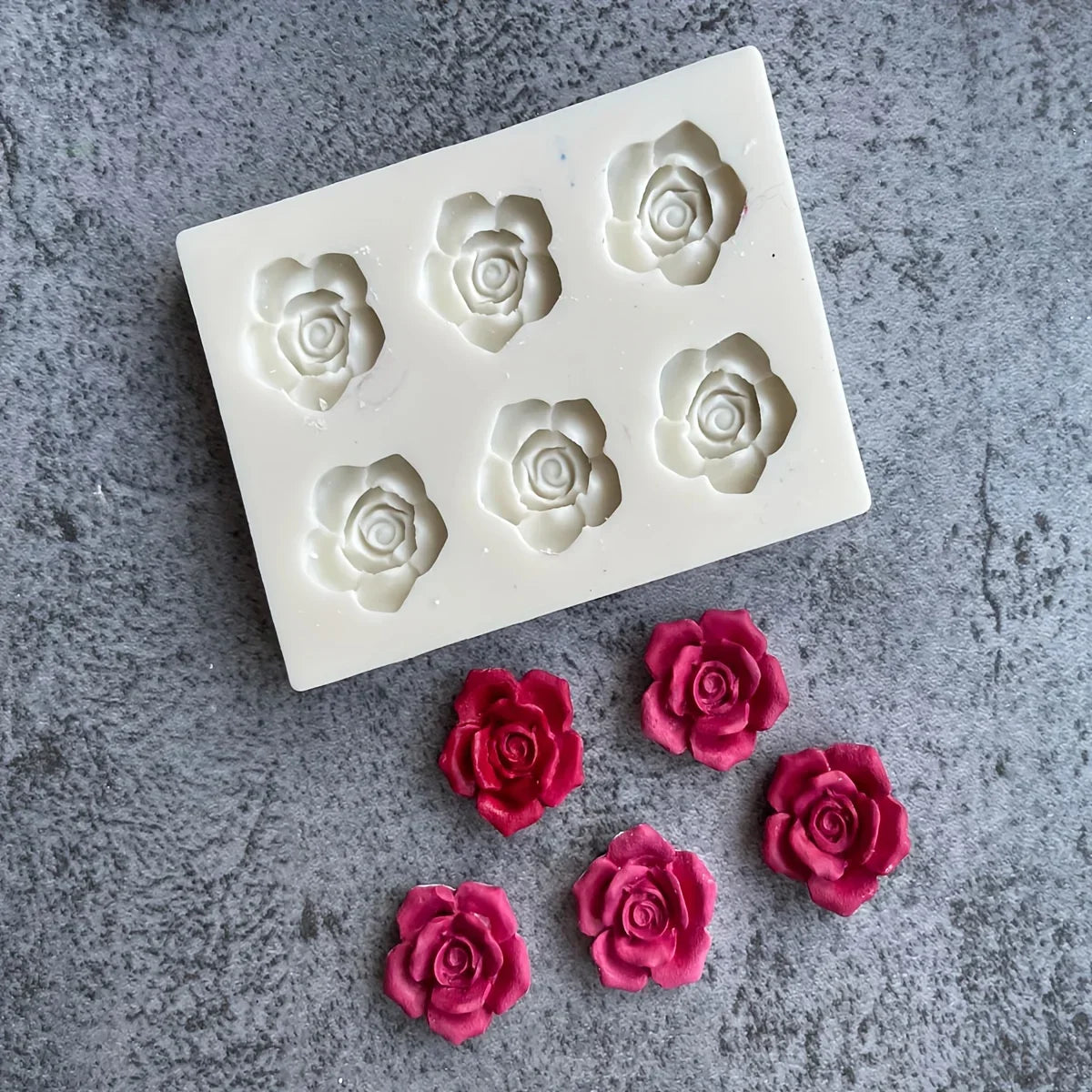 A white silicone mold with six rose flower shapes for candle and soap making is displayed on a gray surface.