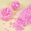 A collection of pink plastic beads and filler material scattered on a light background.