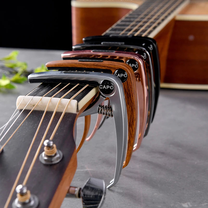 Close-up of a professional metal guitar capo with pick holder and tuning pegs on a wooden guitar neck.