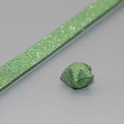 A strip of green glitter origami star paper is shown next to a finished green origami star.