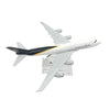A white diecast model of a Boeing airplane with black and yellow accents, shown in flight.