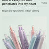 A collection of nine colored gel pens in various shades of pink, purple, and blue are displayed in a clear glass container.