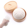 A light beige dumpling squishy stress ball is shown being removed from its round, fluted container.