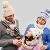 A woman is holding a child and wearing knitted winter accessories, including a hat and scarf.