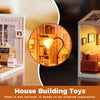 A wooden miniature house kit showing a cozy living room interior with furniture and lighting.