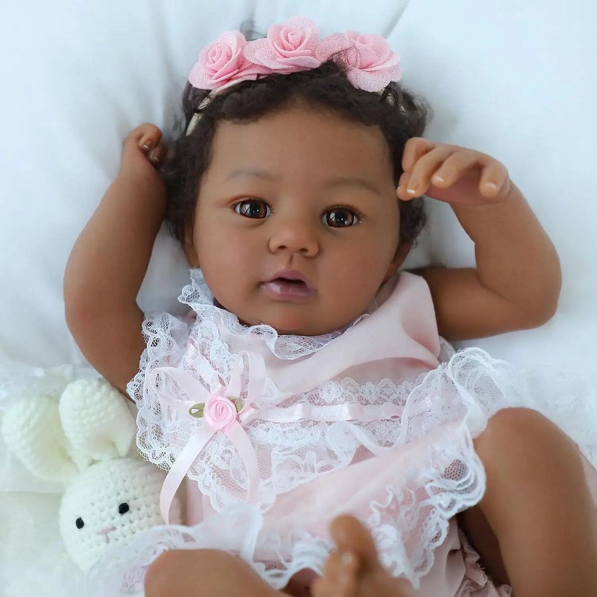 A close-up of a lifelike reborn baby doll named Abigail with soft body, wearing a pink lace outfit and a pink floral headband