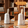 A white vertical sewing machine spool holder with a thread guide is shown on a wooden table.