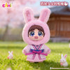 A plush blind box of a rabbit-eared girl in pink attire with a pink hood standing in a grassy outdoor setting.