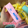 A hand holds a pink butter stick squishy stress ball next to several yellow butter sticks.
