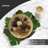 A bowl filled with various natural-looking brown and beige decorative leaves and spherical elements on a white marble surface