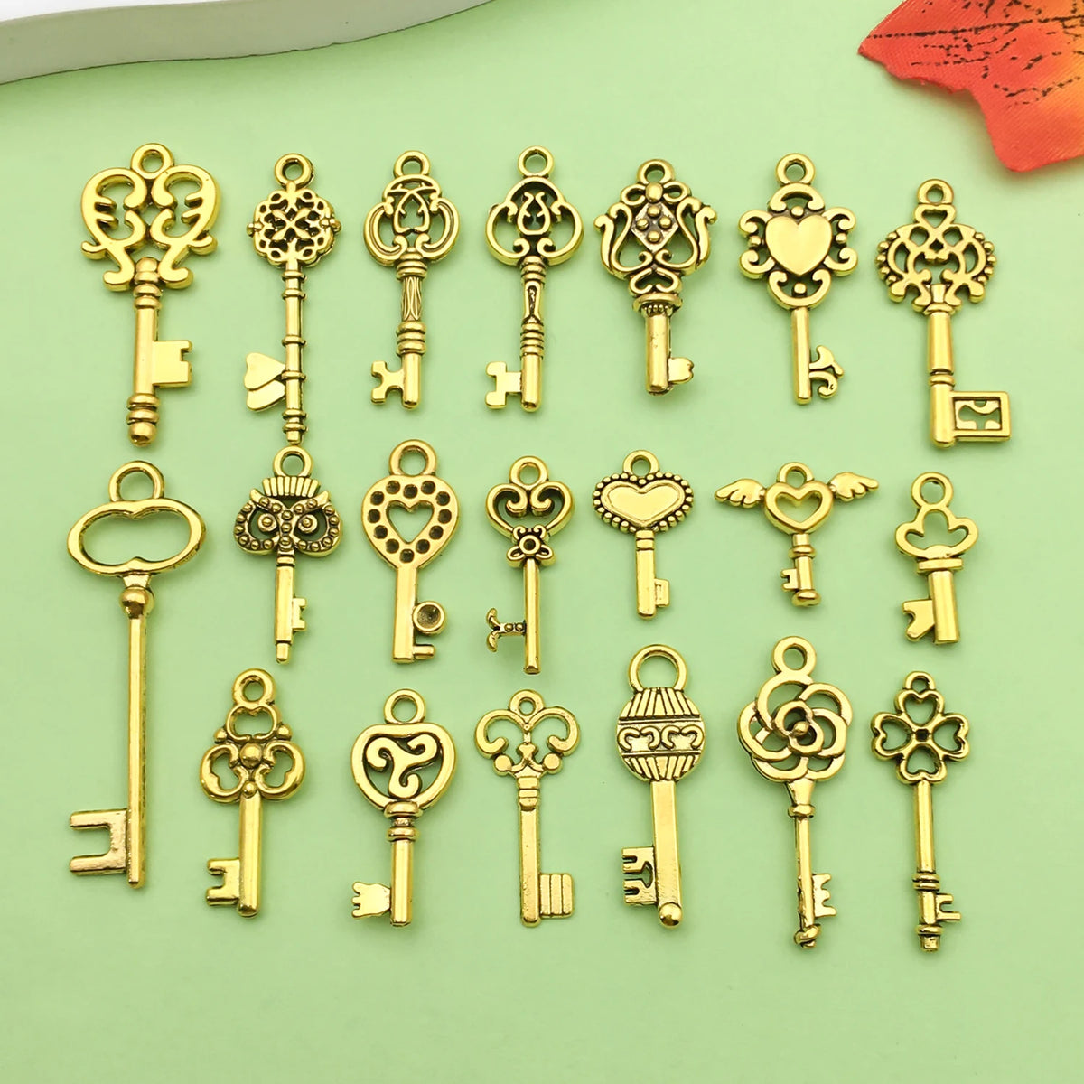 A collection of vintage gold-toned key charms and pendants for jewelry making displayed on a light green surface.