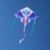 Une figure ressemblant à un dragon bleu aux ailes violettes volant une aile de delta en nylon contre un ciel bleu clair.
