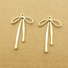 A pair of gold-colored alloy bow charms for jewelry making displayed on a brown surface.