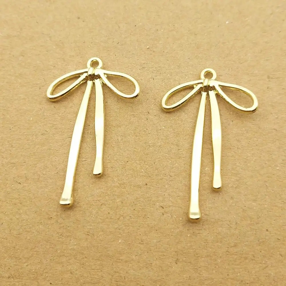A pair of gold-colored alloy bow charms for jewelry making displayed on a brown surface.