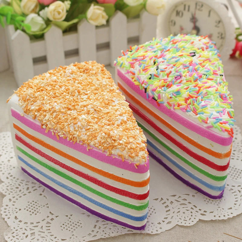 A colorful rainbow layer cake squishy toy with striped frosting and sprinkles resting on a white lace doily.