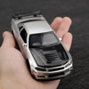 A silver die-cast sports car with a black hood is held in a person's hand.