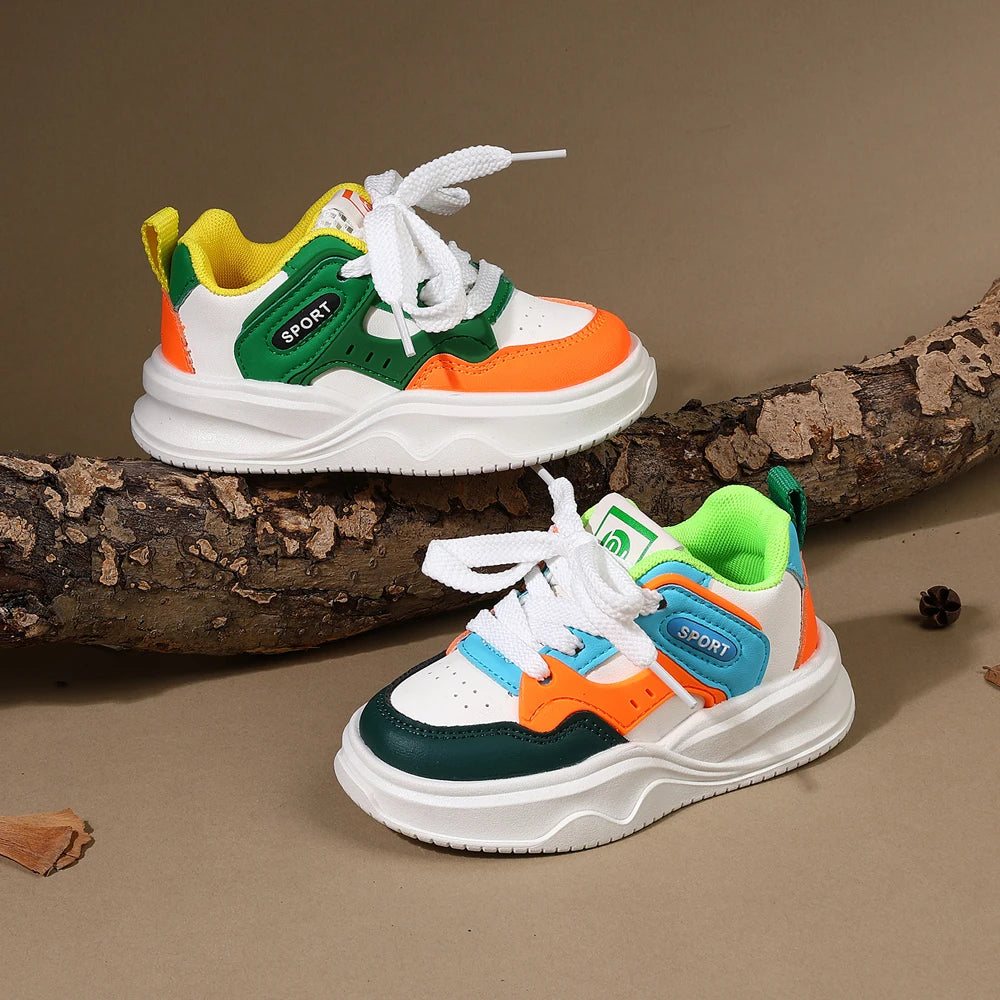A pair of yellow, green, and orange casual sneakers with white laces and thick soles resting on a brown tree branch.