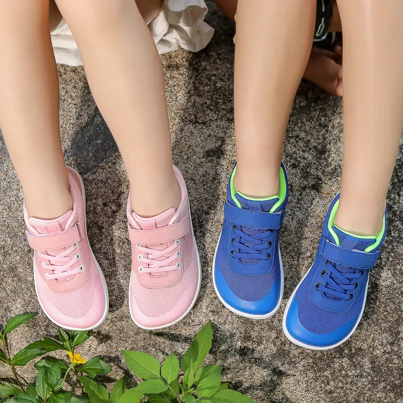 A pair of pink and blue kids barefoot training sneakers are shown on a textured gray surface.