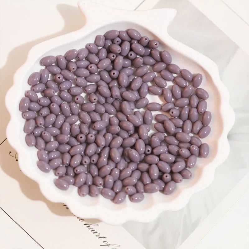 A pile of purple oval glass rice grain beads for jewelry making in a white dish.