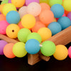 A collection of glow-in-the-dark silicone beads in various bright colors are displayed on a wooden surface.