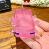 A pink squishy fidget toy shaped like a small creature with purple accents is held in a hand.