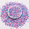 A pile of colorful polymer clay slice sprinkles in various shades of pink, blue, and white scattered on a white surface.
