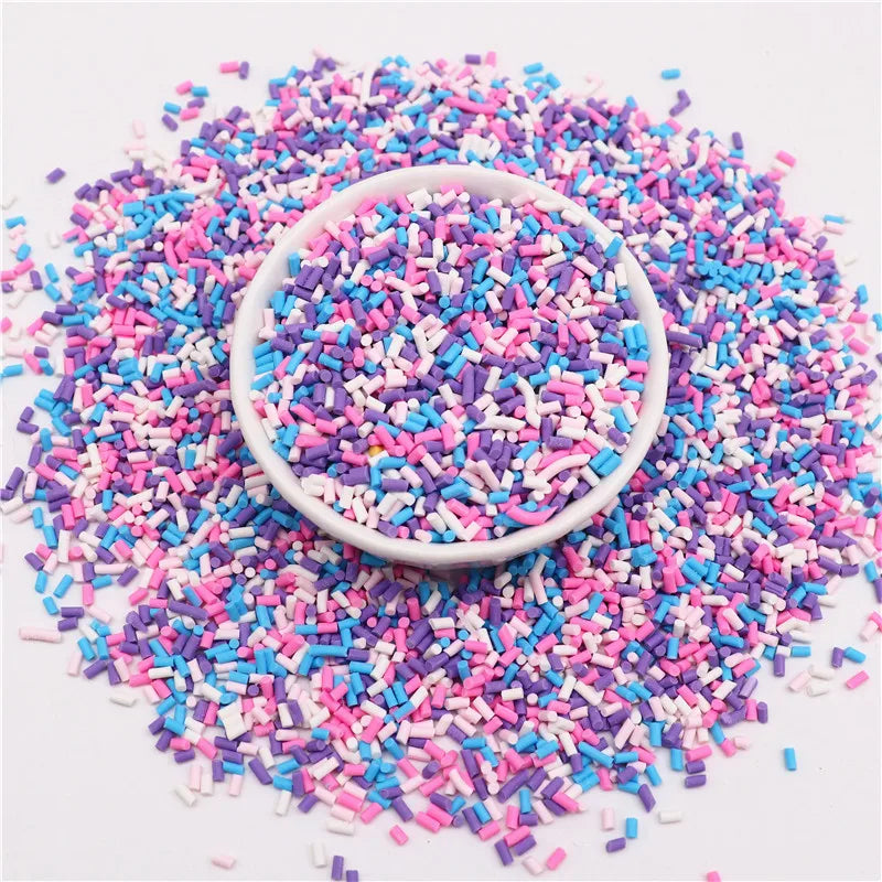 A pile of colorful polymer clay slice sprinkles in various shades of pink, blue, and white scattered on a white surface.