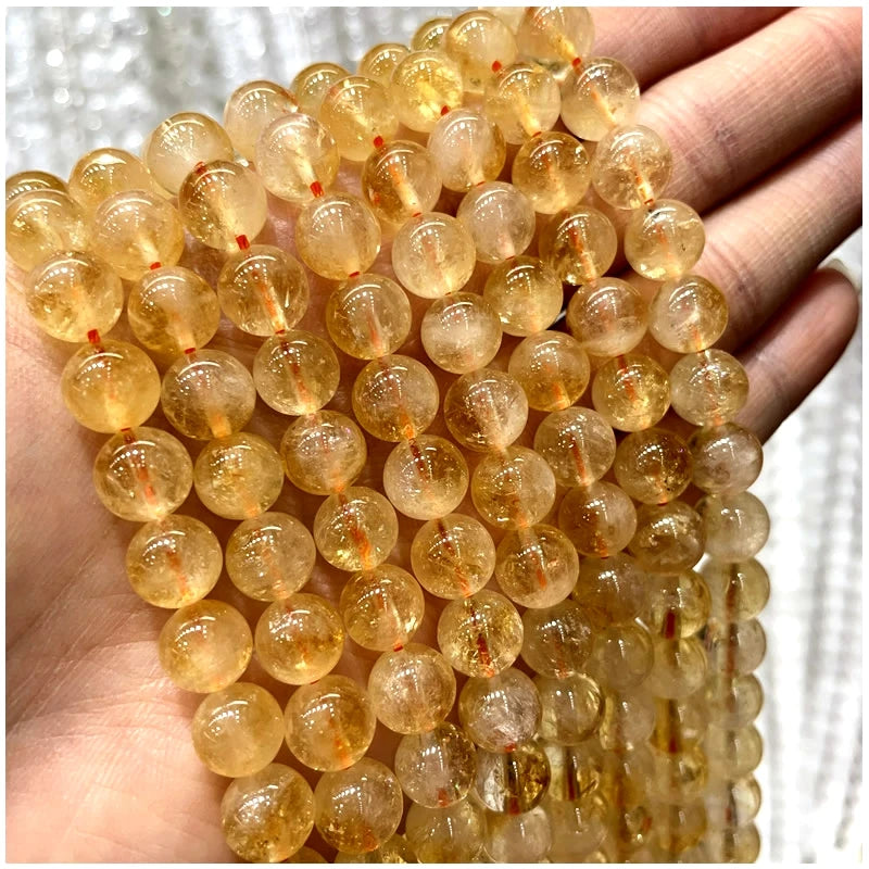 A hand holds a string of small, translucent yellow-orange natural stone beads for jewelry making.