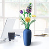 A vase filled with a floral bouquet made of building blocks featuring purple and yellow flowers on a white desk.